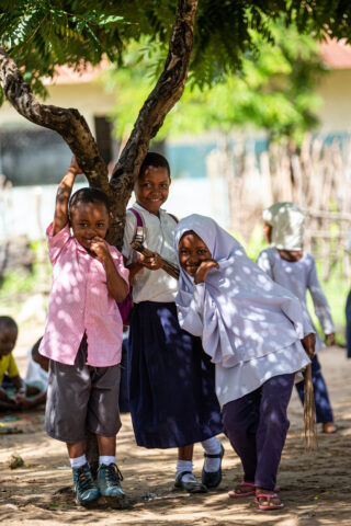 Three smiling children next to a small tree