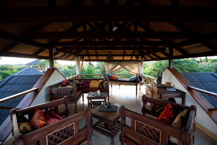 The roof terrace of one of the bungalows with a great view of the surrounding vegetation, featuring chairs, a sofa, a desk, and an outdoor bed with mosquito net